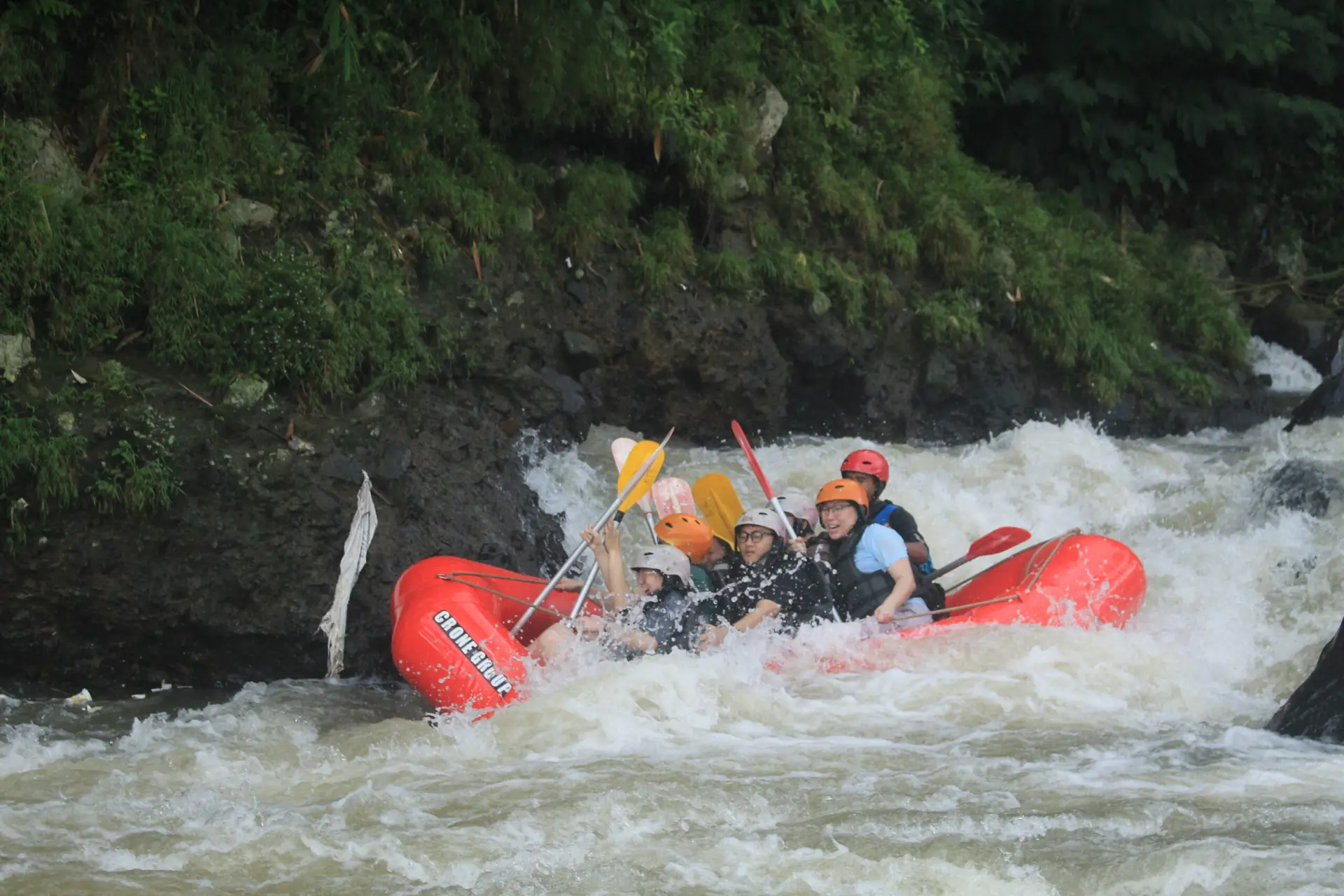 Perahu merah menembus jeram deras diapit tebing bervegetasi lebat