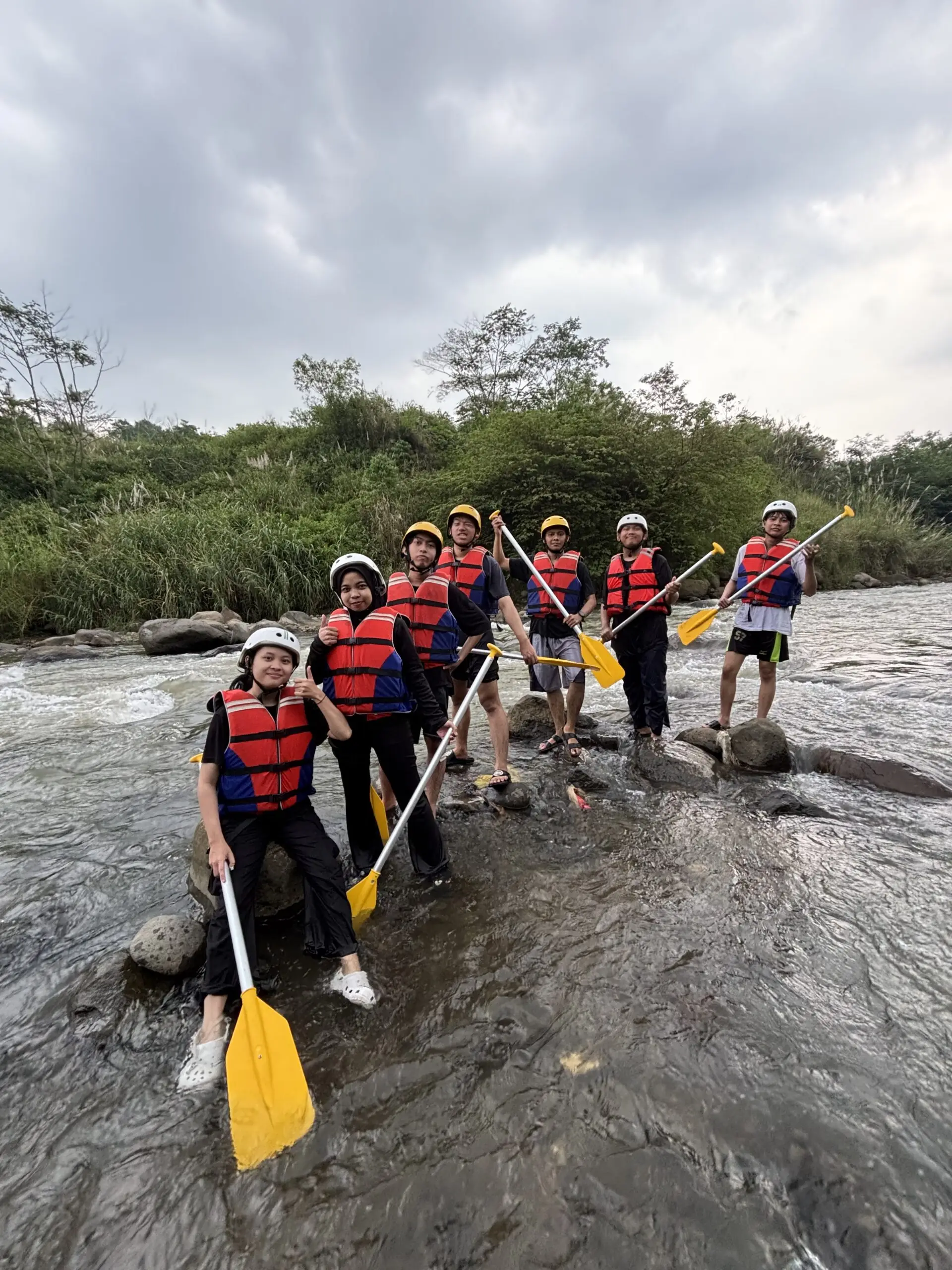 Tim berdiri di bebatuan sungai dengan pelampung dan dayung